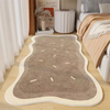 A rectangular beige area rug with light brown accents and a white border placed on a light wood floor.
