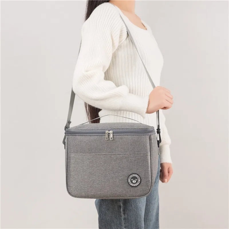 A woman is holding a gray thermal insulated lunch bag with an adjustable shoulder strap.