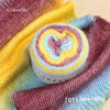 A roll of colorful gradient cake yarn in various shades of yellow, pink, and blue wool-blend for knitting and crochet.