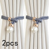 A set of two pearl and rope curtain tie-backs with gold accents against a light beige curtain.