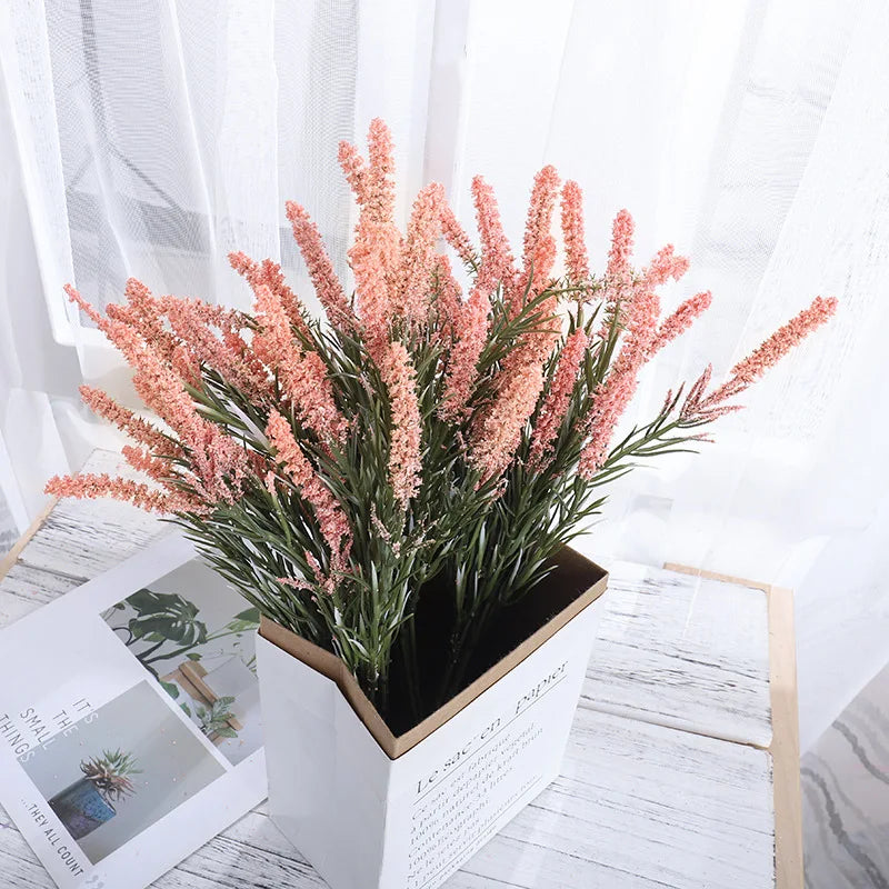 Ein Strauß pinker künstlicher Lavendelblüten in einem quadratischen Holztopf auf einer weißen Oberfläche.