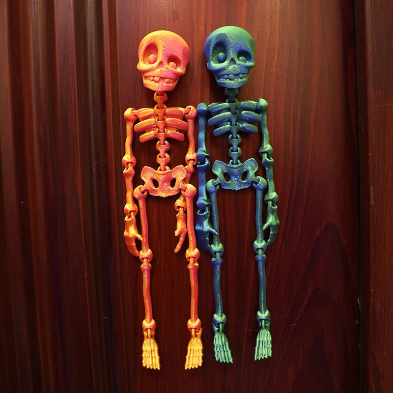 Two poseable luminous skull fridge magnets, one orange and one blue, displayed against a dark wooden background.