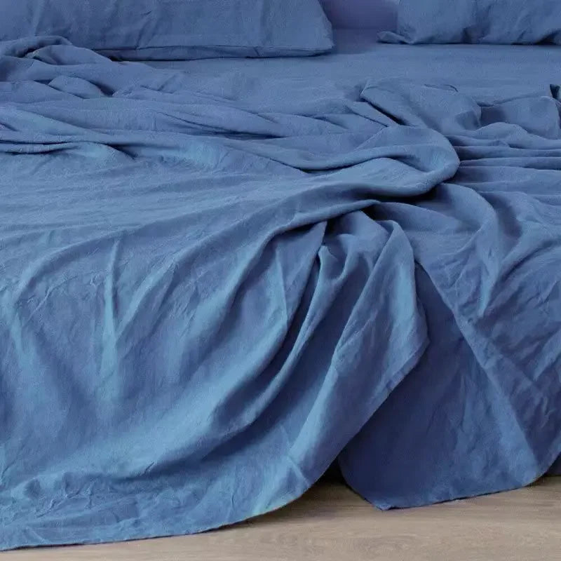 A soft blue pure linen bed sheet set draped on a bed with pillows.