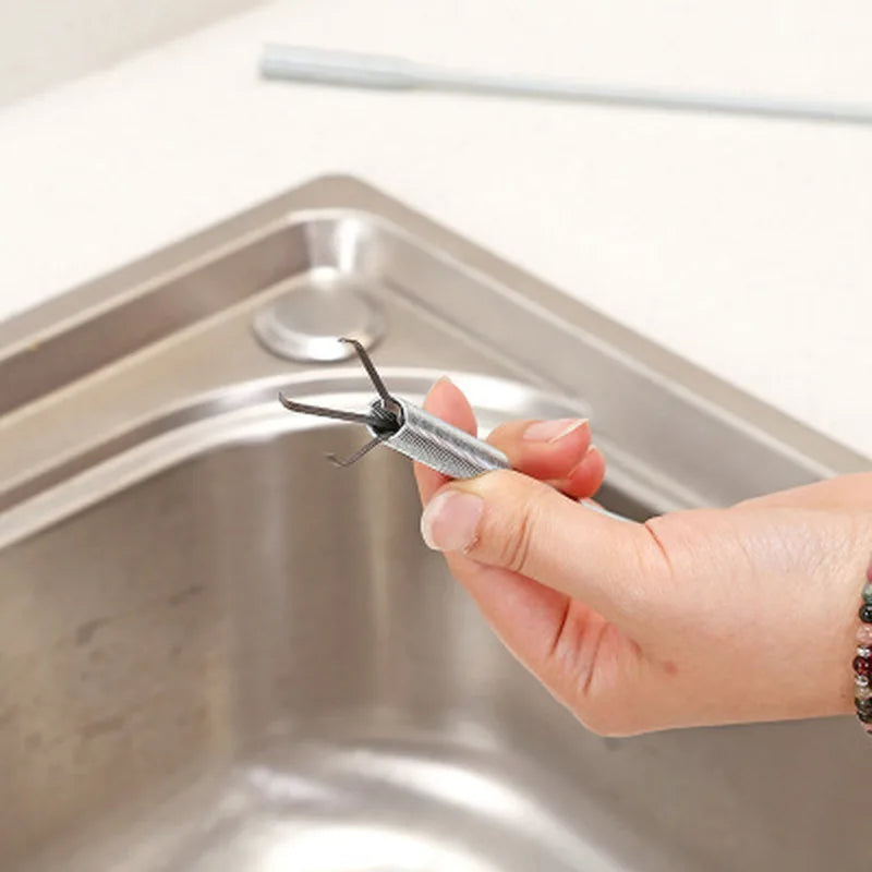Une main tient un serpent de nettoyage de drains métallique avec une pointe en griffe sur un évier de cuisine en acier inoxyd