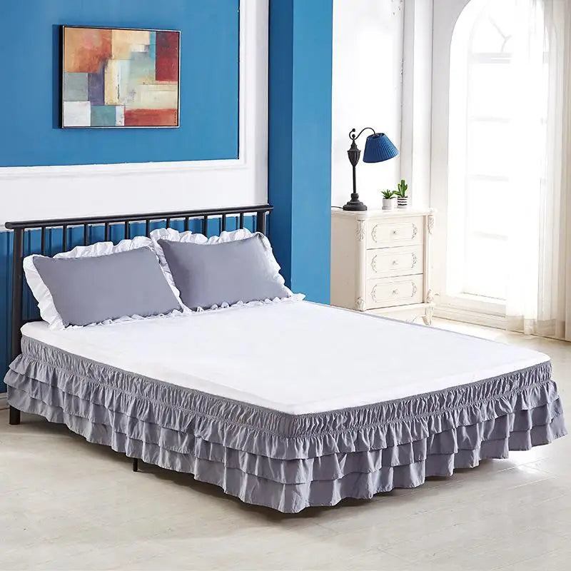 A white bed with a gray ruffled skirt and light blue walls and artwork.