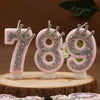 Three pink rhinestone crown number candles for birthday cakes, numbered 789, displayed on a wooden surface.