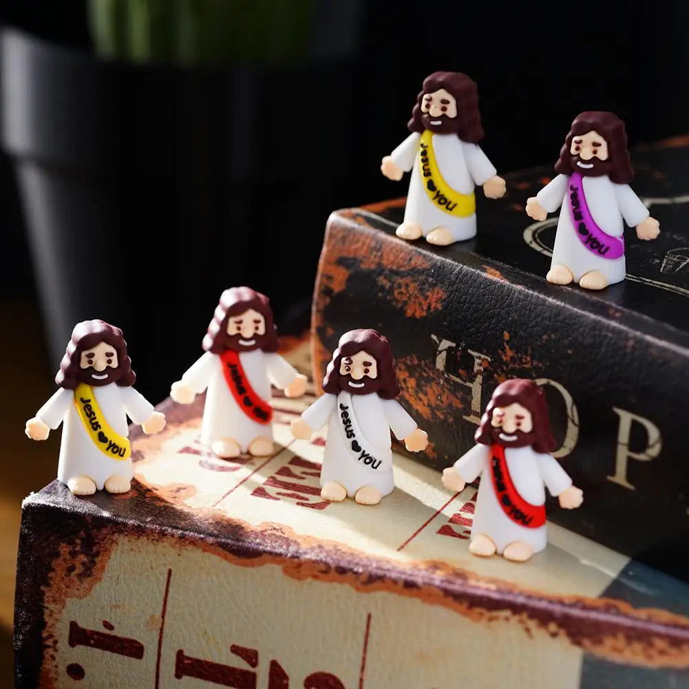 A set of mini Jesus figurines with long brown hair and white robes displayed on a stack of old books.