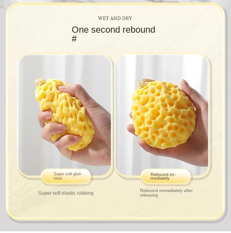 A hand is squeezing a yellow soft mesh bath sponge ball, demonstrating its rebound property.