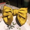 A bright yellow silk bow hair clip used as a ponytail holder, displayed on a white surface.