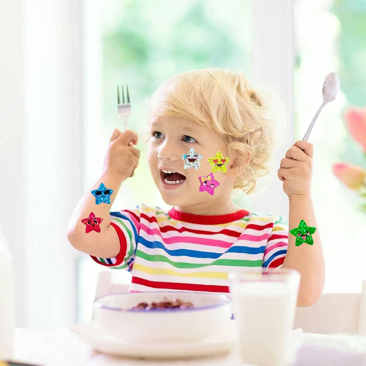 A blonde toddler holds up his hands decorated with glitter star stickers while eating at a table.