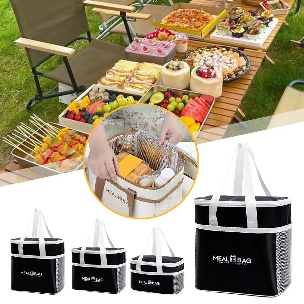 A set of black insulated lunch bags with white handles and a logo, shown next to a spread of food.