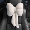 A white plush bowknot car headrest pillow with neck support resting on a black leather seat.