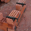 A black brick liner puller tool is shown pulling a wire through the gaps of red clay bricks on a reddish ground.