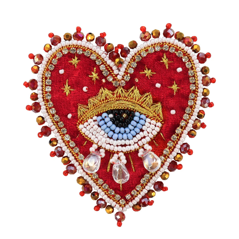 A heart-shaped patch made of red fabric and adorned with sparkling beads, rhinestones, and a gold eye design.