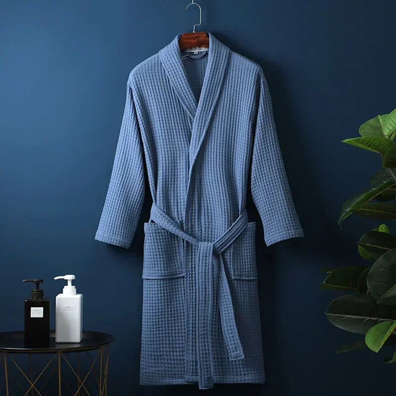 A light blue waffle knit robe hanging on a wooden hanger against a dark blue wall.