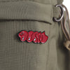 A red bubble enamel pin brooch with the text MF DOOM is attached to a military green fabric.