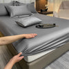 Vista cercana de un juego de sábanas ajustadas de algodón gris de lujo, drapeado sobre una cama, con almohadas y accesorios v
