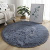 A round, fluffy gray shaggy rug placed on a light wooden floor in a living room setting.