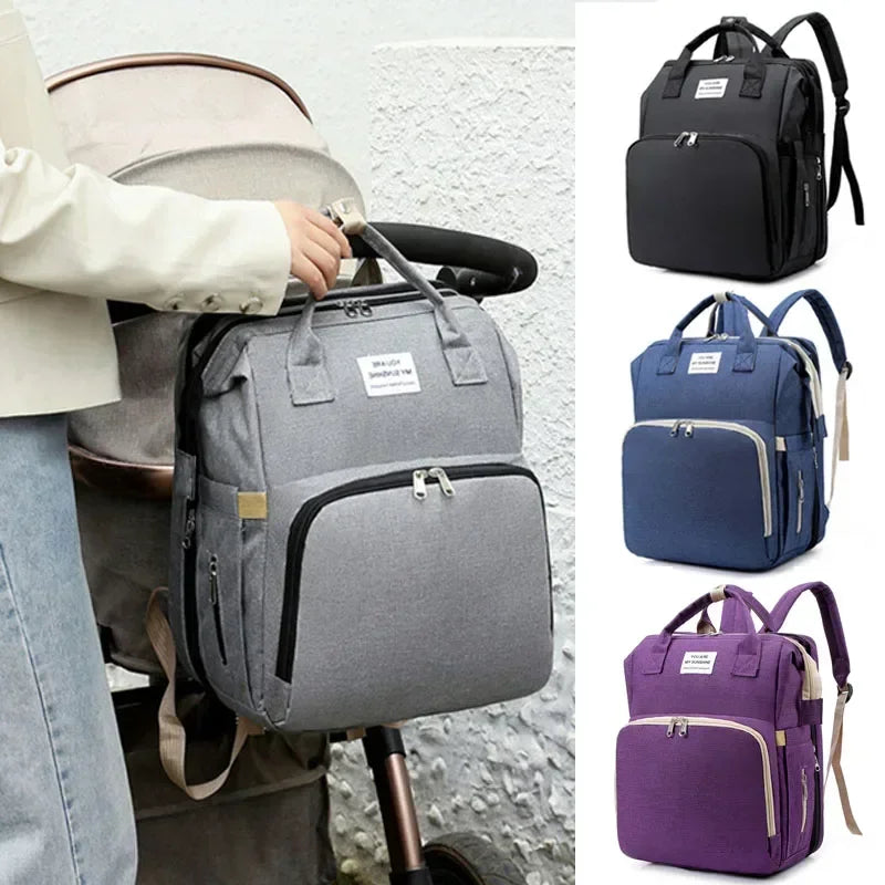 A collection of gray and blue diaper bags and backpacks displayed next to a person holding one.