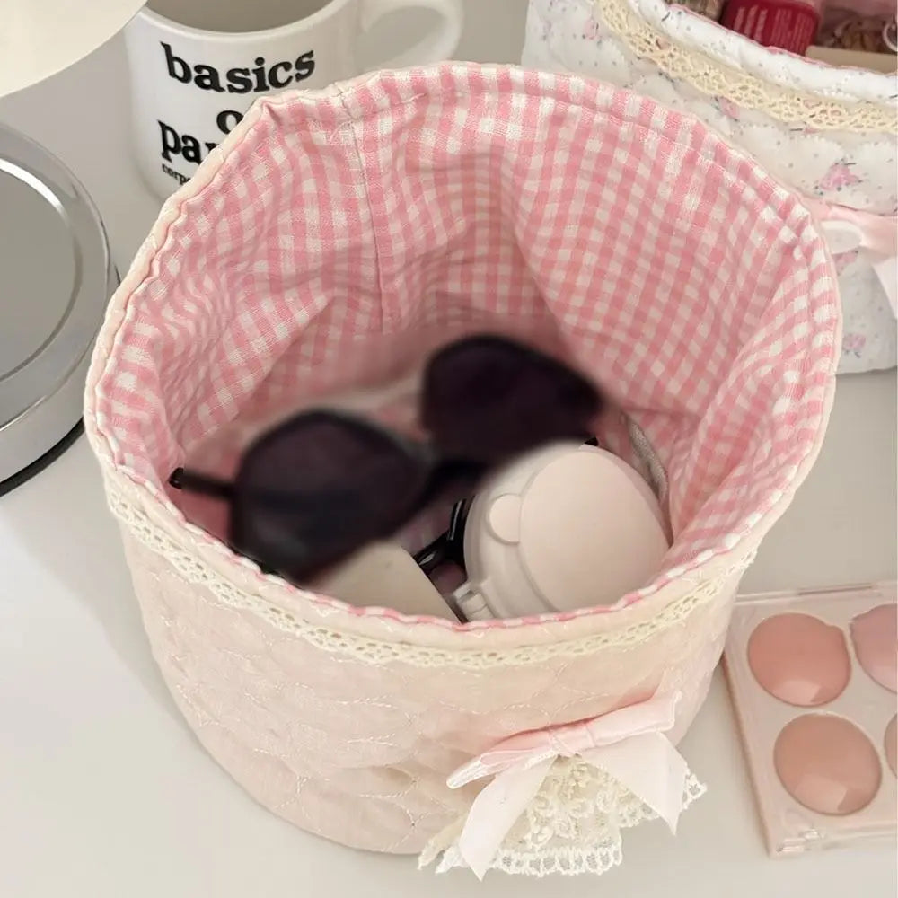 Cesta de acolchado en forma de corazón rosa llena de objetos redondos claros y una cinta rosa.