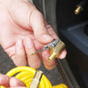 A hand holds a brass tire inflator chuck with a quick-connect clip near a yellow hose.