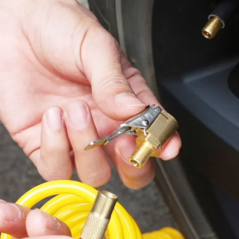 A hand holds a brass tire inflator chuck with a quick-connect clip near a yellow hose.