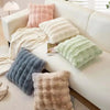 A collection of fluffy decorative pillows in shades of pink, cream, and gray resting on a white sofa.