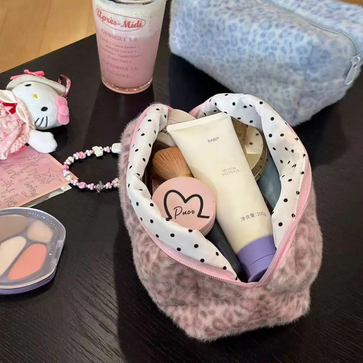 A pink leopard print cosmetic bag with a plush lining containing various beauty products and a glass of liquid.