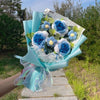 Ein Bouquet handgefertigter Häkelblumen in Blau- und Weißtönen, in hellblauer Papier umwickelt.