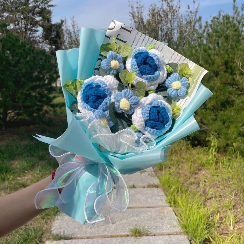 Ein Bouquet handgefertigter Häkelblumen in Blau- und Weißtönen, in hellblauer Papier umwickelt.