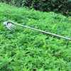 A stainless steel gardening hook with a fork end and a long handle is shown against a background of green foliage.