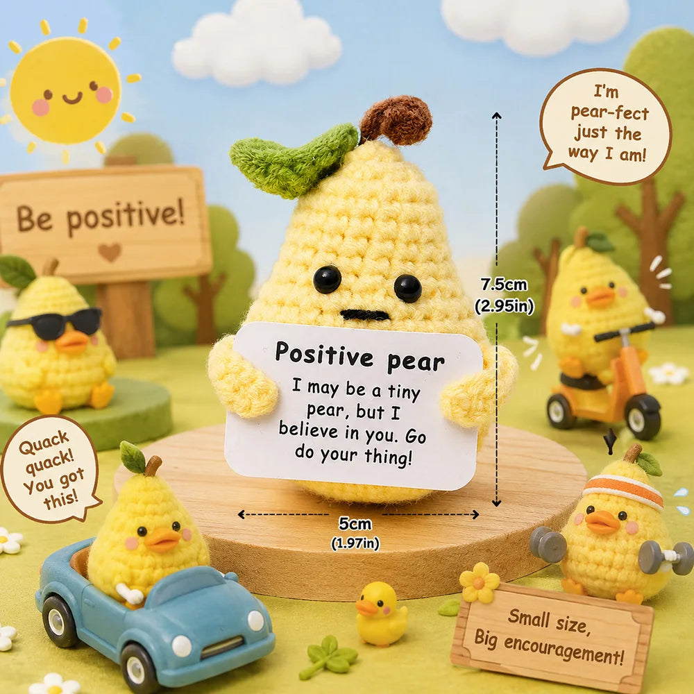A yellow crochet pocket hug doll sits on a wooden surface surrounded by small plants and encouraging signs.