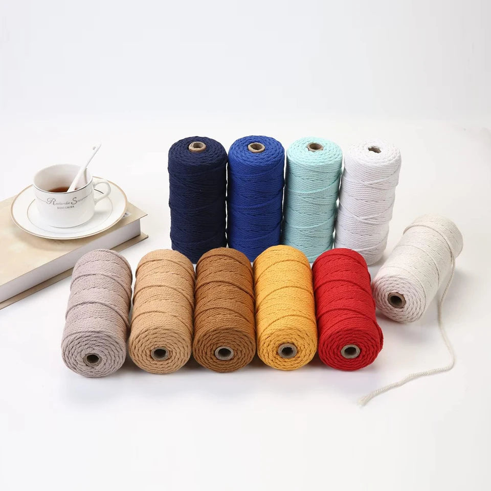 A collection of spools of 100% cotton macrame cord in various colors including blue, teal, white, and natural beige.