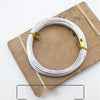 Silver anodized aluminum jewelry wire coiled on a wooden board with natural twine.