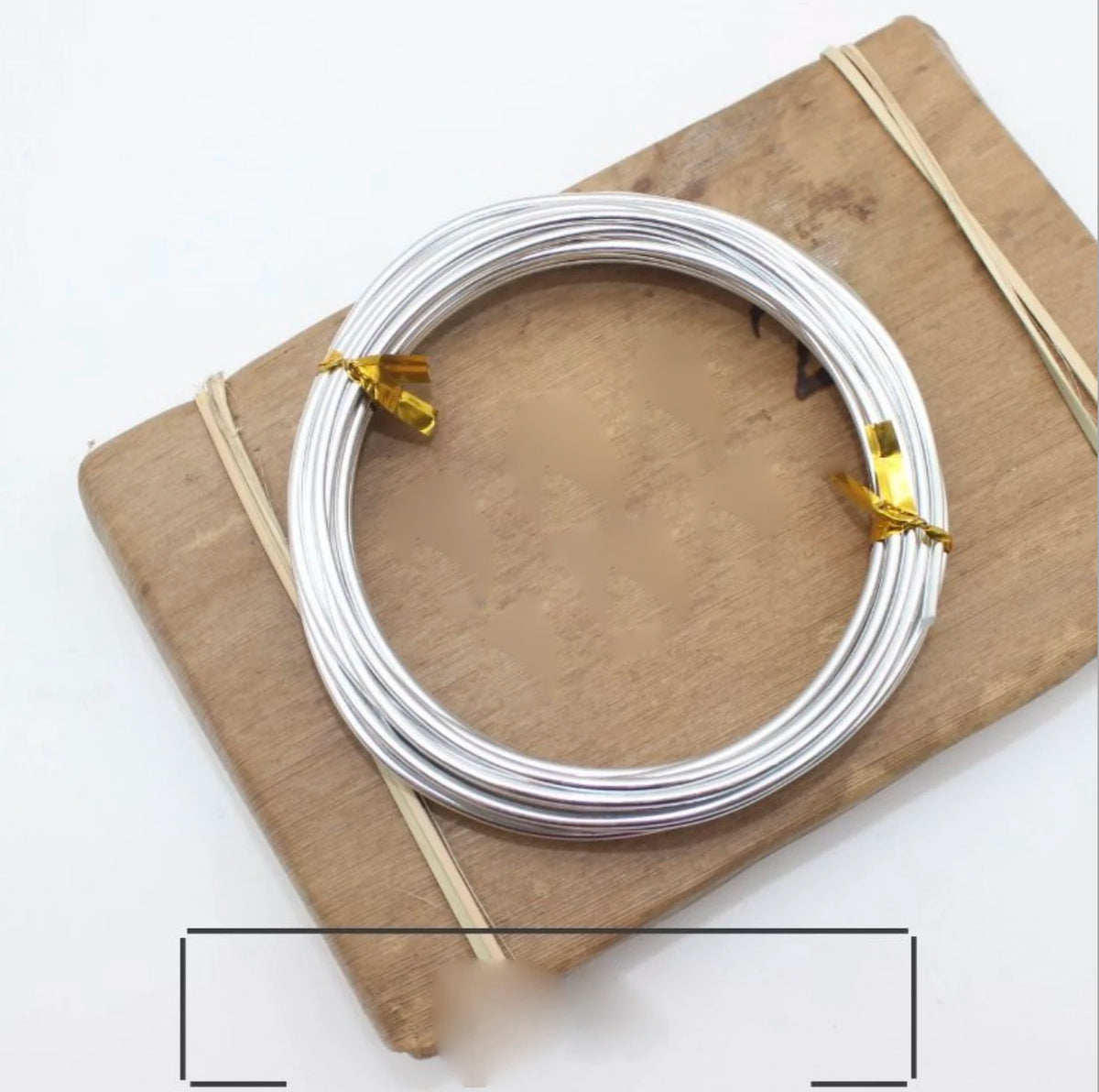 Silver anodized aluminum jewelry wire coiled on a wooden board with natural twine.