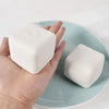 A hand holds a white squishy milk tofu stress relief fidget toy on a light blue plate.