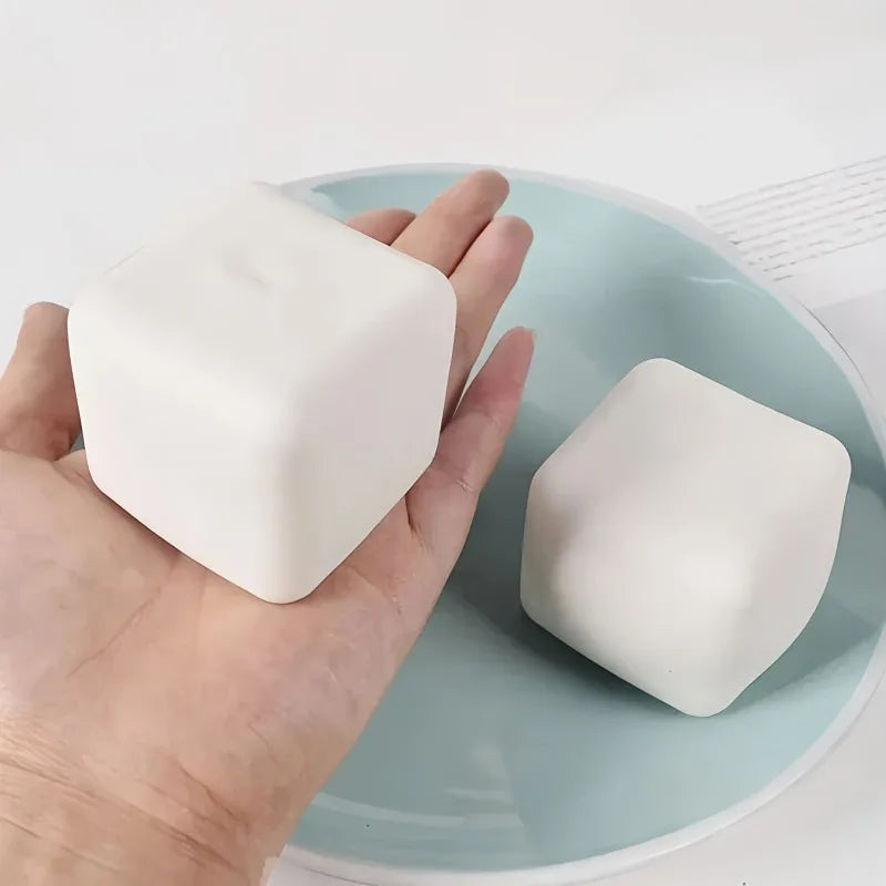 A hand holds a white squishy milk tofu stress relief fidget toy on a light blue plate.