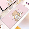 A pink kawaii cartoon desk mat featuring a teddy bear and a kitten, displayed next to a laptop.