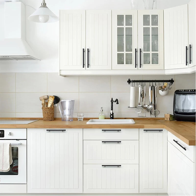 Weiße Küchenschränke mit gebürstetem Nickel und goldenen Grifflern über einer Holz-Arbeitsplatte.