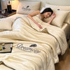 A woman rests under a cream-colored comforter featuring embroidered text on the fabric.