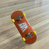 An orange skateboard with a wooden fingerboard and realistic yellow trucks resting on a light wood surface.