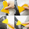 A hand is using a yellow vinyl wrap application tool to apply film onto a surface.