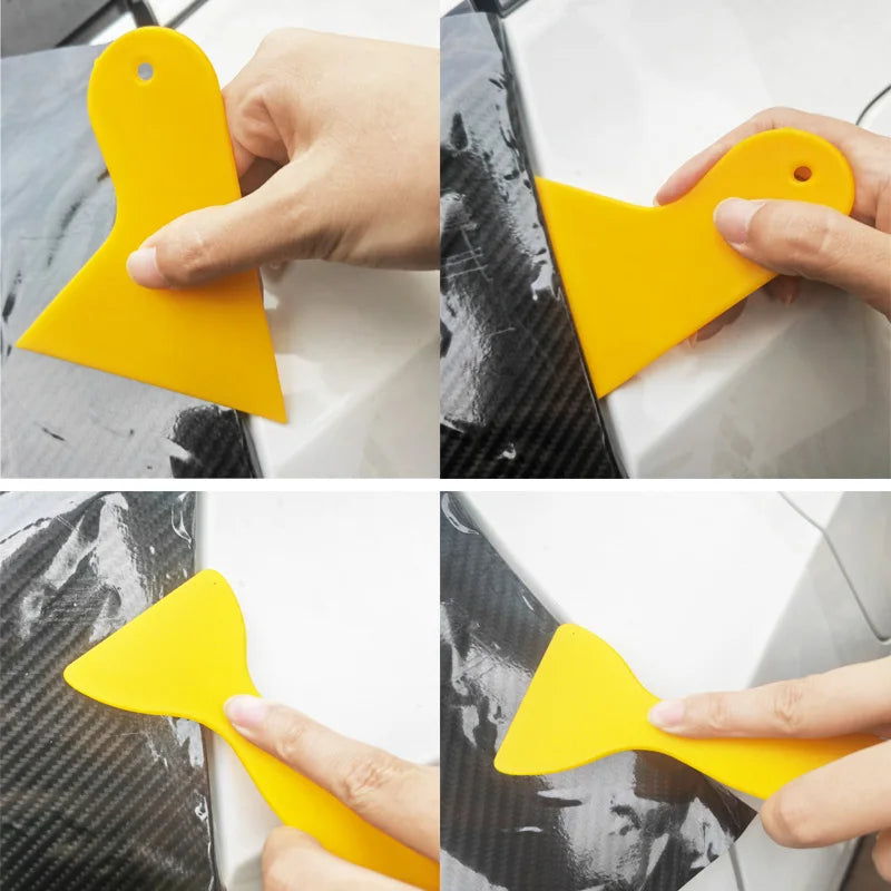 A hand is using a yellow vinyl wrap application tool to apply film onto a surface.
