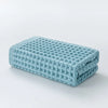A stack of light blue waffle weave bath towels folded on a white surface.