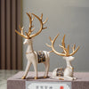 A set of two resin deer figurines with golden antlers and decorative patterns, displayed on a gray surface.