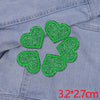A set of five green glitter heart iron-on embroidered patches on a denim fabric.