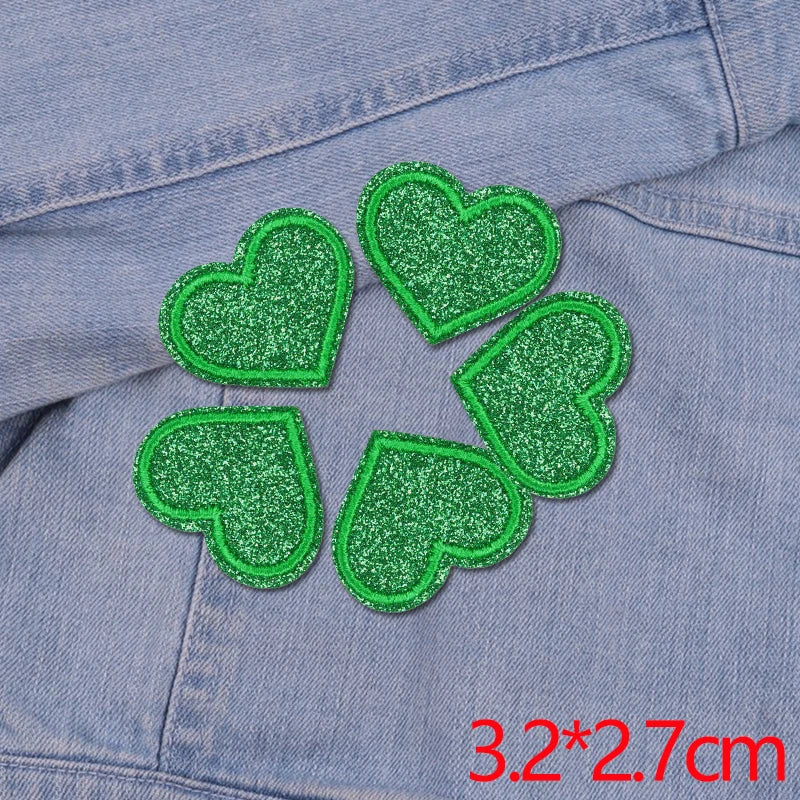 A set of five green glitter heart iron-on embroidered patches on a denim fabric.