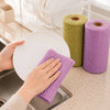 Hands are using a purple reusable tear-away cleaning cloth near a roll of green cloths in a kitchen setting.