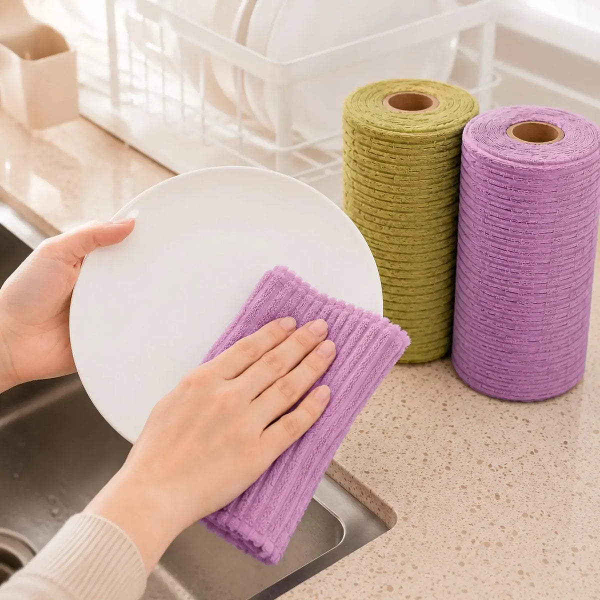 Hands are using a purple reusable tear-away cleaning cloth near a roll of green cloths in a kitchen setting.