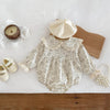 A beige floral lace cotton romper for a baby girl is displayed on a white surface with a wooden board and a light beige hat.